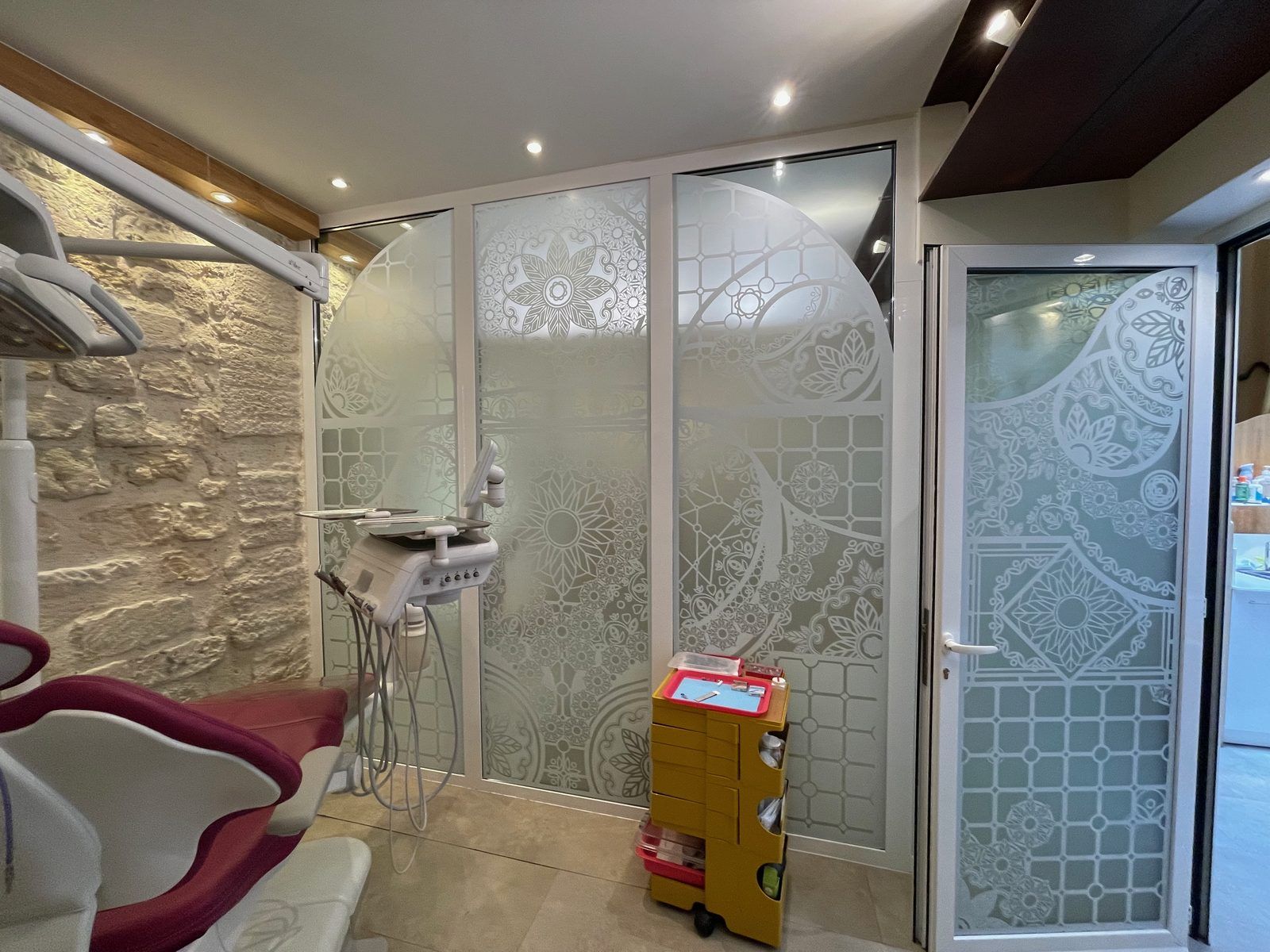 Salle de soins du cabinet dentaire avec cloisons vitrées décorées et mur en pierre apparente